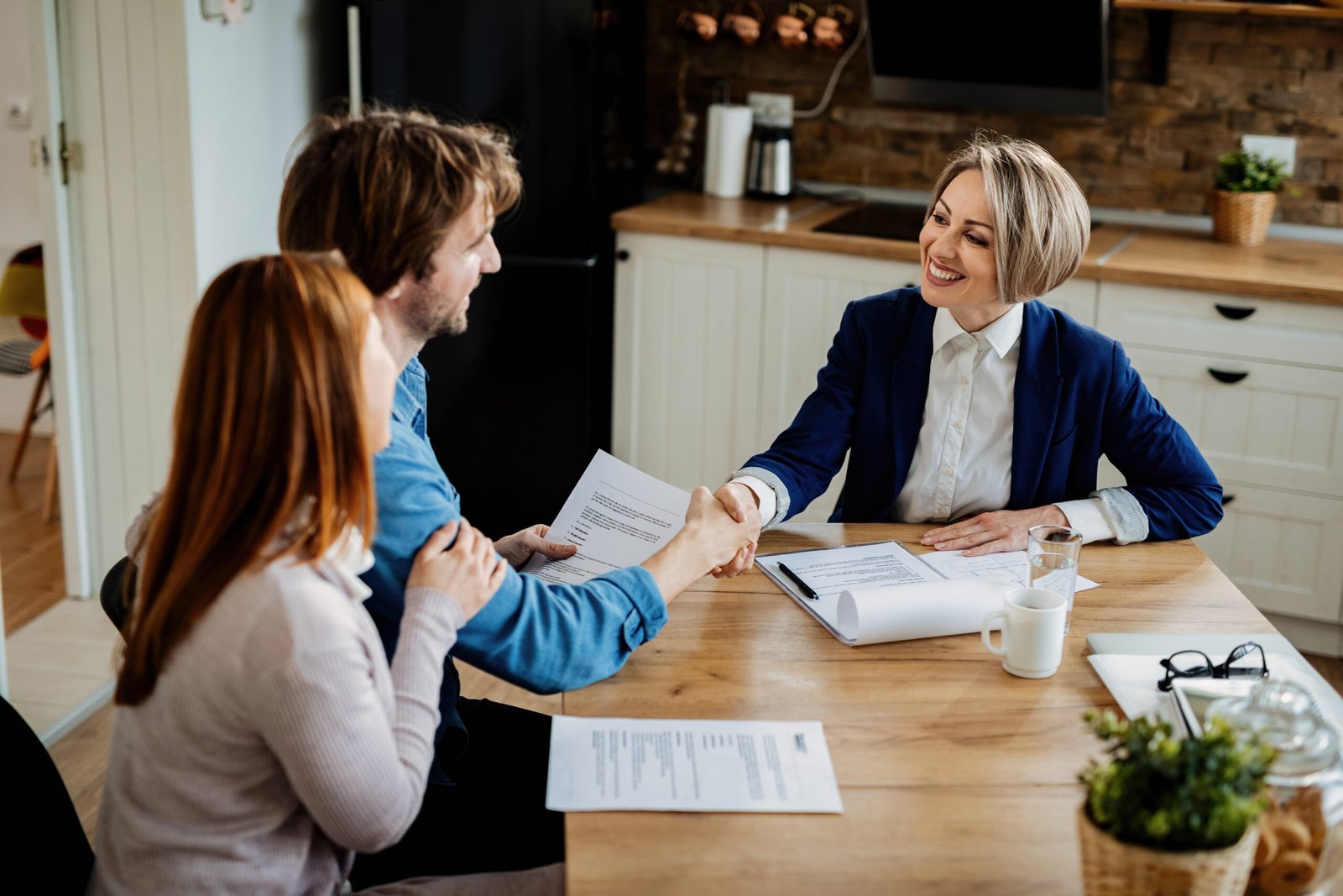 Happy insurance agent shaking hands with young couple after successful meeting.